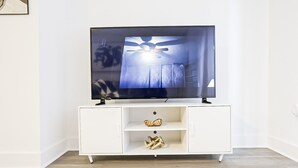 Un meuble de rangement blanc pour appareils électroniques, doté d’un téléviseur à écran plat, de deux étagères et d’un petit objet décoratif.