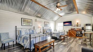 A spacious room with two beds, a wooden bench, a kitchenette, and a ceiling fan.
