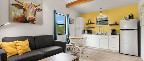 A modern living room with a grey sofa, a wooden coffee table, and a colorful cow painting on the wall.