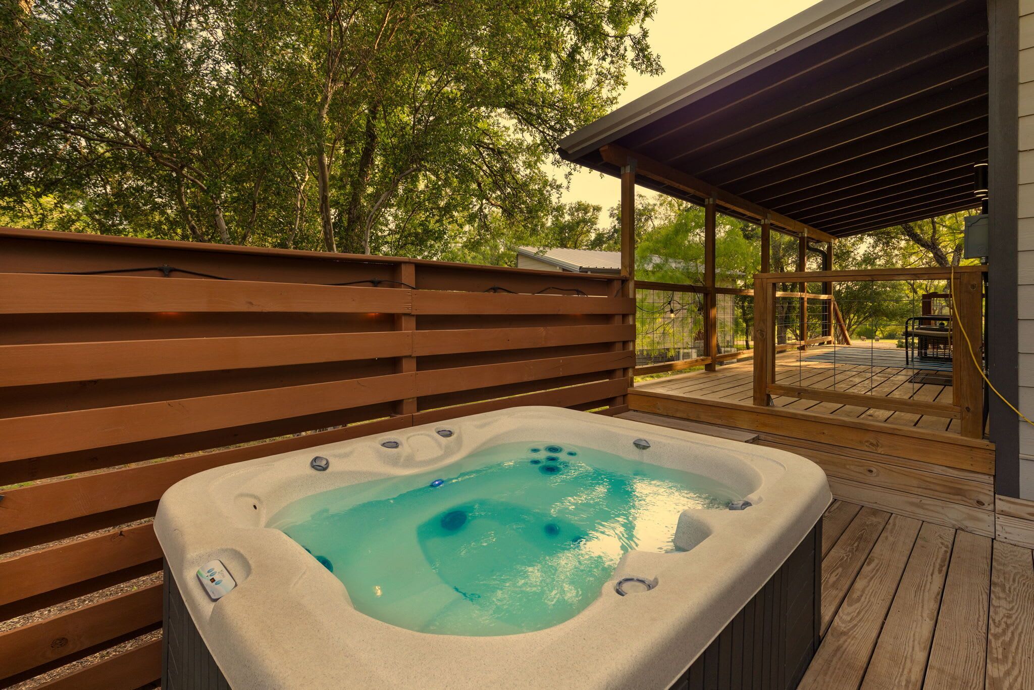 A hot tub on a wooden deck with a wooden fence and a covered area in the background.