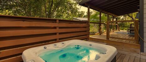 A hot tub on a wooden deck with a wooden fence and a covered area in the background.