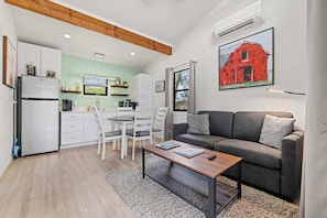 Un salon moderne avec un canapé gris, une table basse en bois et un coin repas comprenant des chaises blanches et un réfrigérateur blanc.