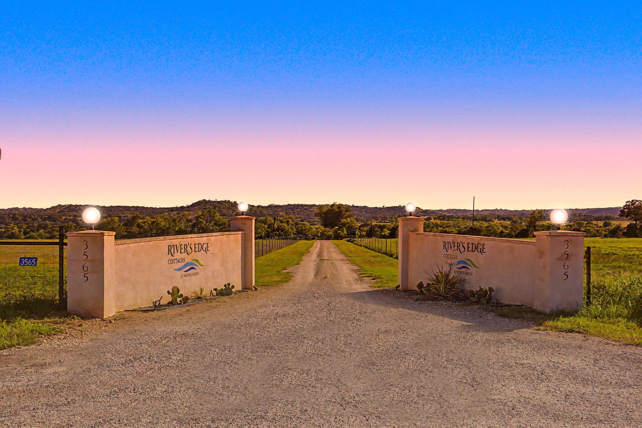 A gravel road leading to a gated entrance with 'River's Edge Cottages' signage.