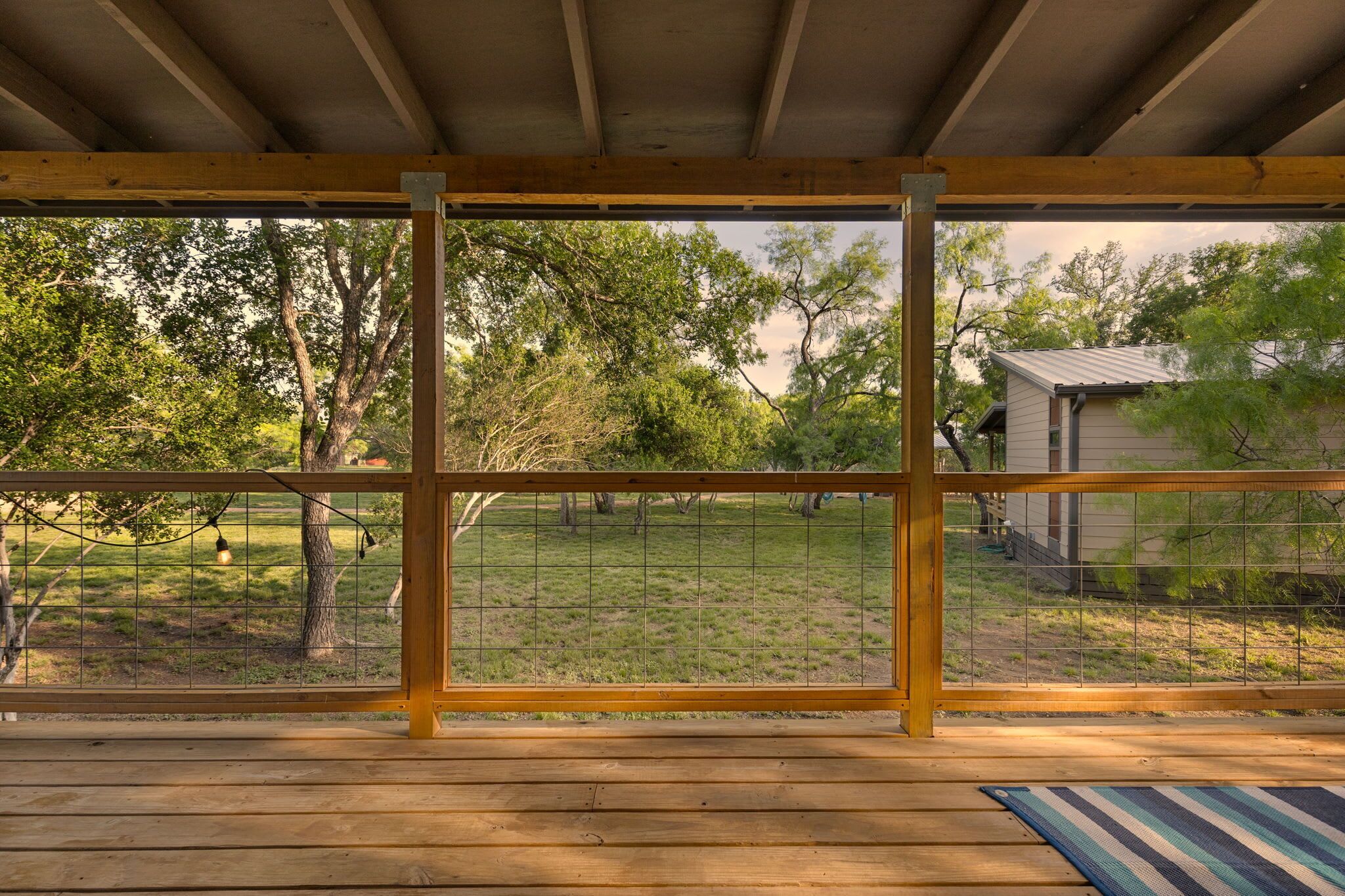 A wooden deck with a view of a grassy yard and trees.