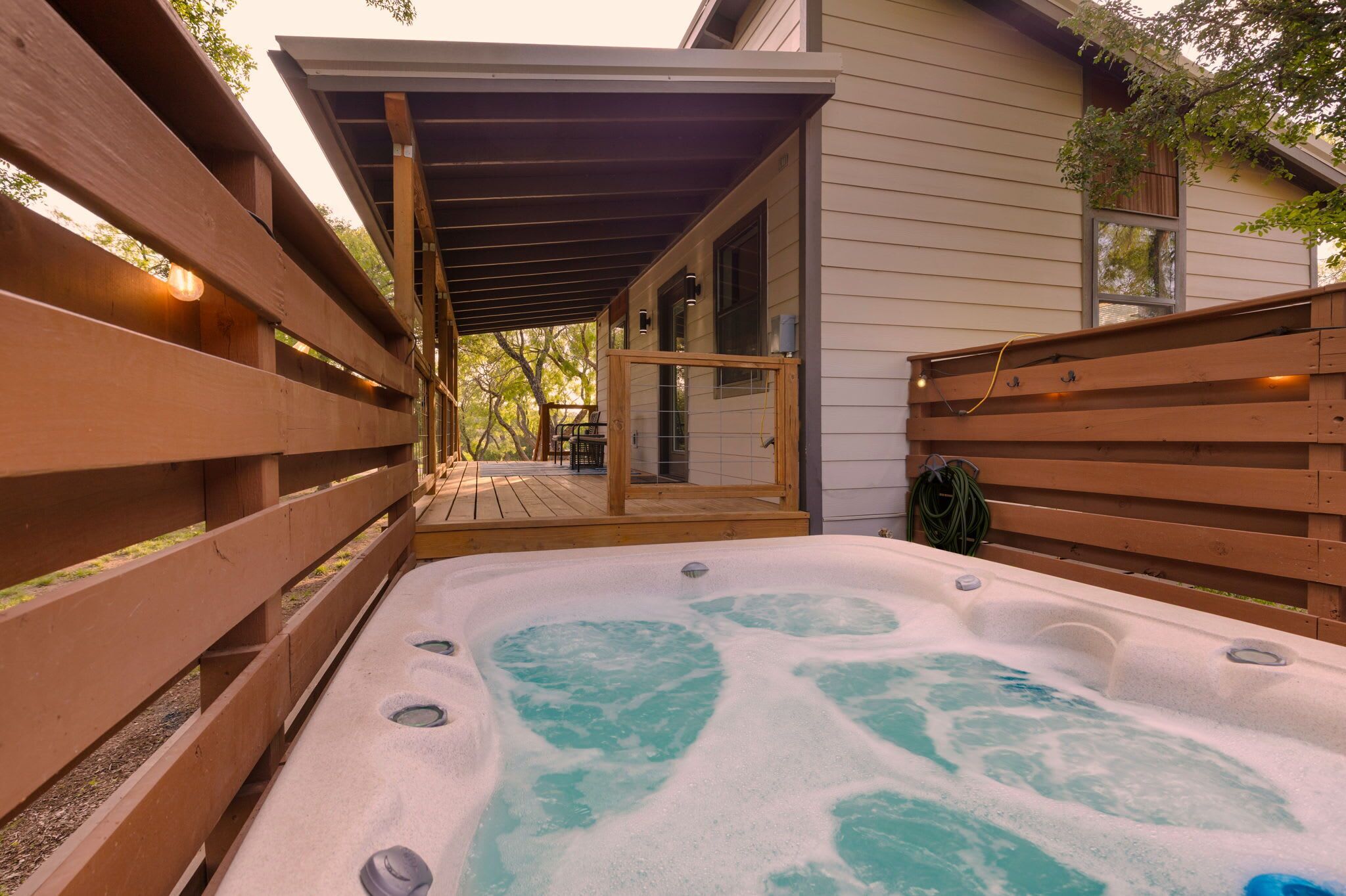 A hot tub with a wooden deck and a covered area, connected to a building with a window and a door.
