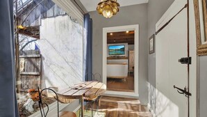 A hallway with a wooden floor, a dining table with chairs, a hanging light fixture, and a television in the background. - Texas Two Step Guesthouse (Fredericksburg)