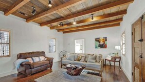 A spacious living room with a high ceiling, wooden beams, a brown leather sofa, a light-colored sofa, a coffee table, and a fan. - Texas Two Step Guesthouse (Fredericksburg)