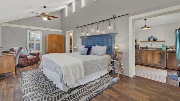 A bedroom with a large bed, a ceiling fan, a wooden wardrobe, a desk, and a chair. - Texas Two Step Guesthouse (Fredericksburg)