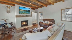 A cozy living room with a fireplace, a leather sofa, a rocking chair, and a mounted deer head. - Texas Two Step Guesthouse (Fredericksburg)