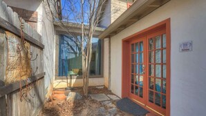 A narrow outdoor corridor with a red door, stone steps, and a small tree. - Texas Two Step Guesthouse (Fredericksburg)