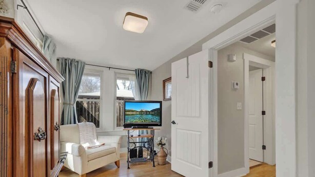 Ein Wohnzimmer mit einem weißen Sofa, einem Fernseher auf einem Schrank, Holzboden und einer Tür zu einem anderen Raum.