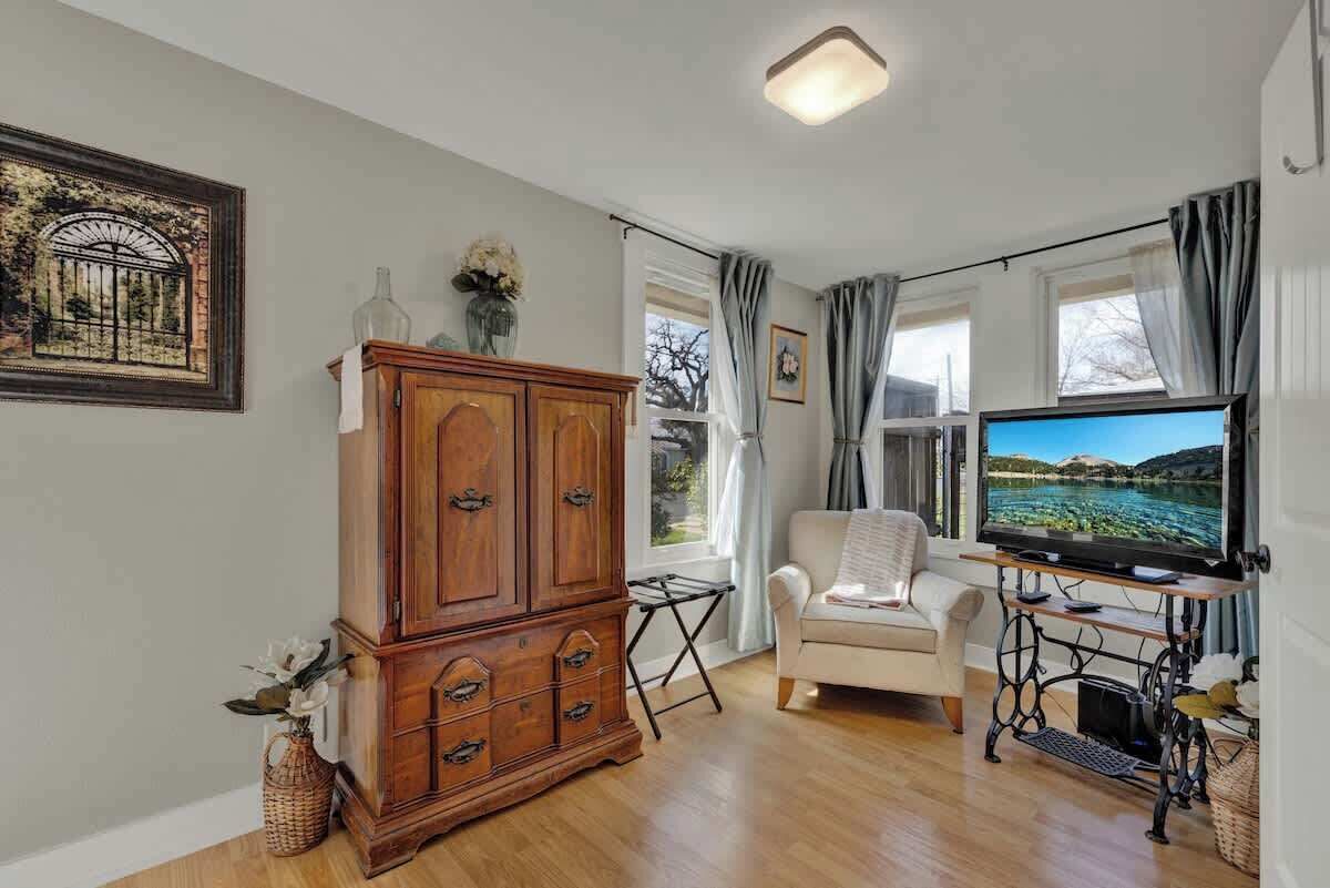 A living room with a wooden cabinet, a white sofa, a television, and a window with curtains.
