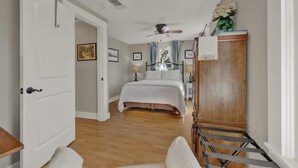 Ein Schlafzimmer mit einem Bett, einem Holzschrank, einem Deckenventilator und einer Tür zu einem anderen Raum.