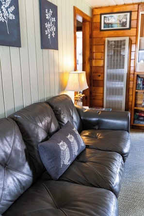 En soffa klädd i läder, tillsammans med en dekorativ kudde, en lampa och en bokhylla, i ett rum med träpanel på väggarna.