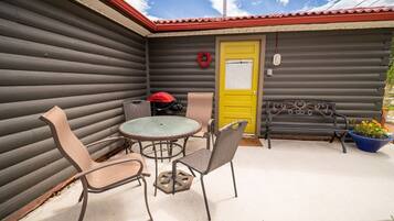 A patio with a round table and chairs, a yellow door, and a red grill.