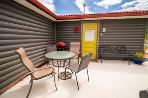 Een terras met een ronde tafel en stoelen, een gele deur en een rode barbecue.