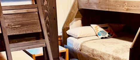 Een stapelbed met een ladder, een klein houten tafeltje en een vloerkleed met een patroon.