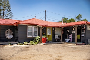A small, single-story building with a red-tiled roof, a porch with a bench, and a number 11 sign on the door.