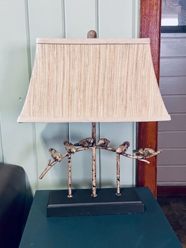 A lamp with a textured lampshade on a stand with branches and birds.