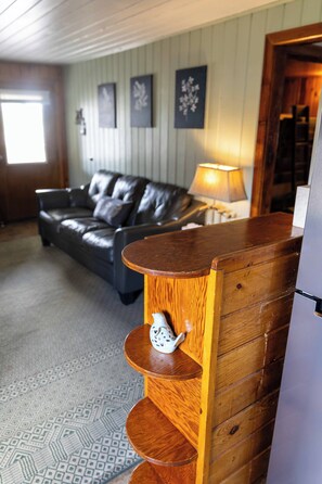 Een woonkamer met een bank, een houten dressoir met planken, een lamp en een koelkast.
