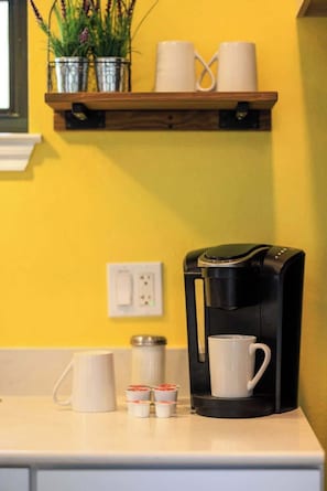A kitchen counter with a coffee maker, white mugs, and a potted plant. - Winecup Waterfront Cottage (Fredericksburg)