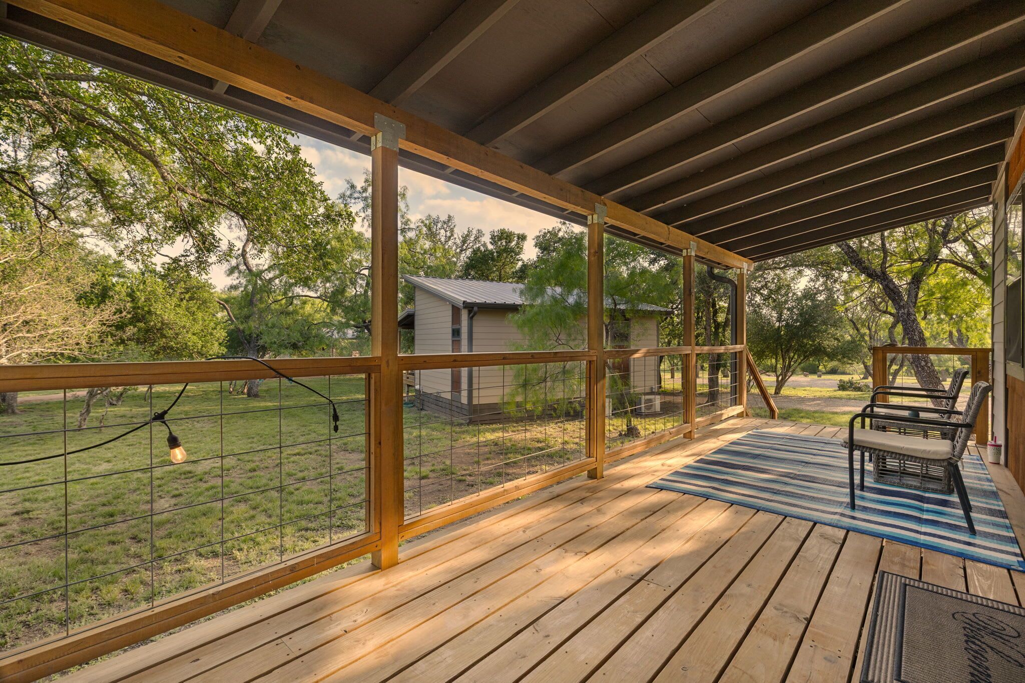 A covered outdoor deck with a view of a fenced yard and trees.