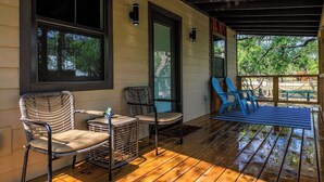 A covered porch with wooden flooring, a seating area with chairs, and a view of the outdoors. - Winecup Waterfront Cottage (Fredericksburg)