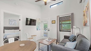 A modern living room with a sofa, a coffee table, a TV, and a door leading to a balcony. - Winecup Waterfront Cottage (Fredericksburg)