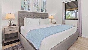 Une chambre à coucher avec un lit, deux tables de chevet, une fenêtre et des œuvres d’art murales.