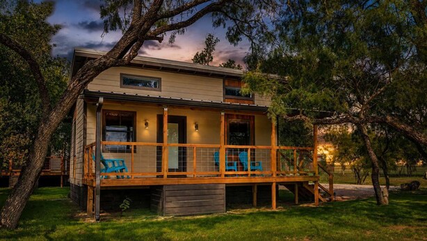 Une maison à deux étages dotée d’une terrasse en bois, d’un porche couvert et d’un petit espace extérieur aménagé pour s’asseoir.