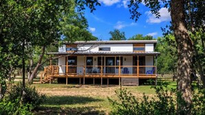 A two-story house with a wooden deck, large windows, and a view of the surrounding greenery. - Rivers Edge Cottages With Hot Tub (Fredericksburg)