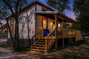 A cabin with a porch, wooden stairs, and a covered seating area. - Rivers Edge Cottages With Hot Tub (Fredericksburg)