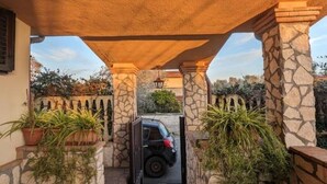 Une allée couverte, bordée de piliers en pierre, avec une voiture garée et des plantes en pot.