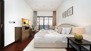 A hotel room with a large bed, a desk, a television, a balcony with a view, and a window with curtains.