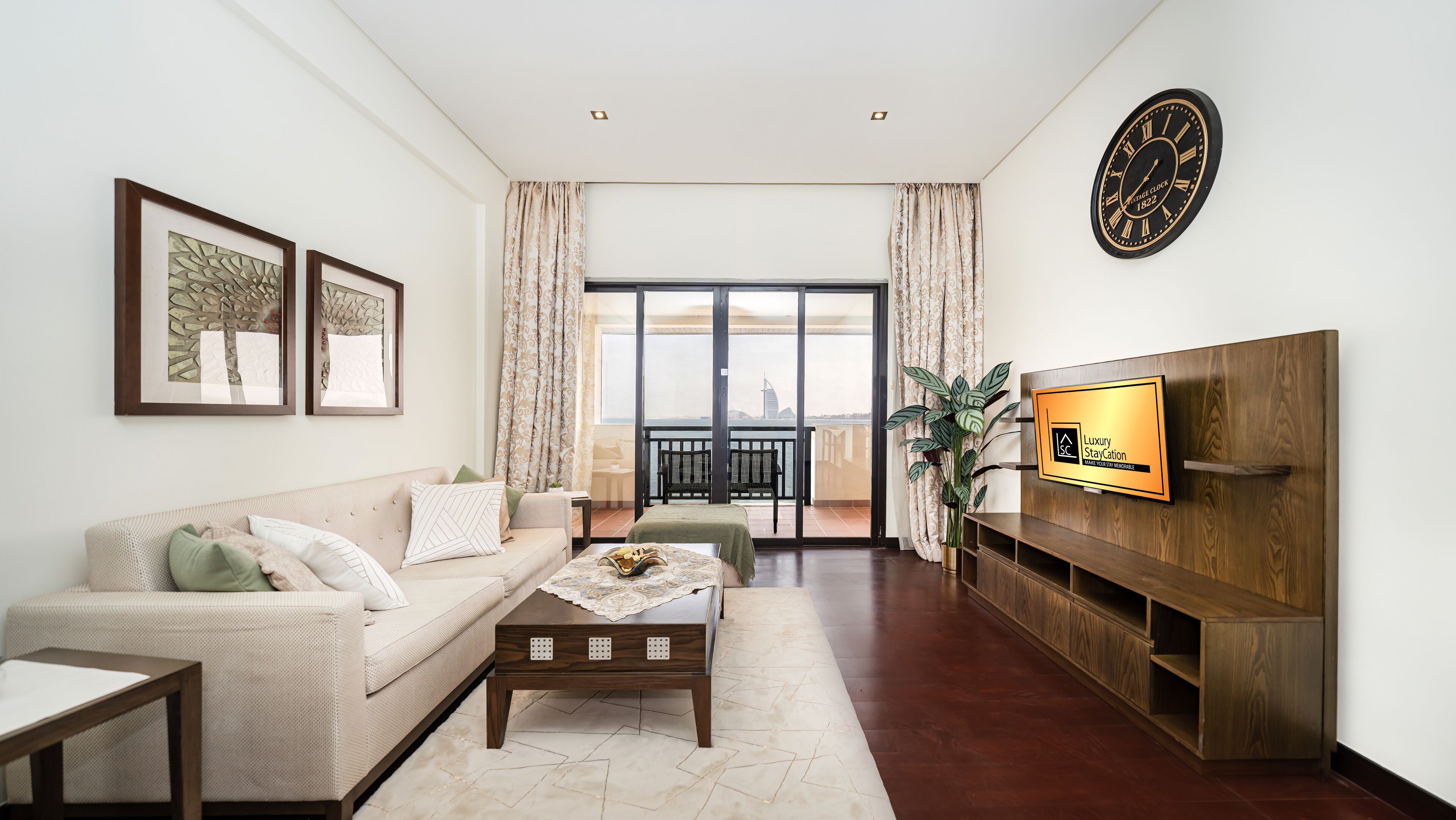 Een moderne woonkamer met een bank, salontafel en televisie. Er is een balkon met gordijnen en uitzicht op de stad.