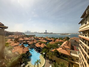 A resort with a swimming pool, beachfront views, and a city skyline in the background. - Luxury StayCation - Exquisite 1BR with Stunning Views on Palm Jumeirah (Dubai)