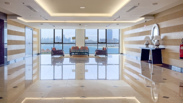 A spacious lobby with a high ceiling, large windows offering a city view, a seating area with two sofas, and a small table with lamps.