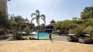 A pool area with lounge chairs and palm trees, surrounded by buildings with tiled roofs.