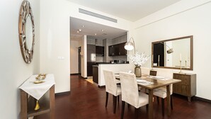 A modern dining area with a wooden table, white chairs, and a vase of flowers. A kitchen is visible in the background.
