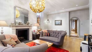 A living room with a fireplace, grey sofas, a coffee table, and a red rug. - Stunning 3 bed flat in the heart of Chelsea (London)