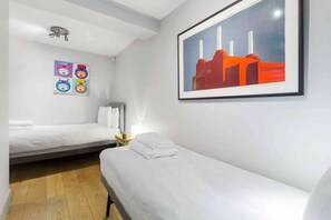 A hotel room with two beds, a wall-mounted artwork, and a small table with a lamp.