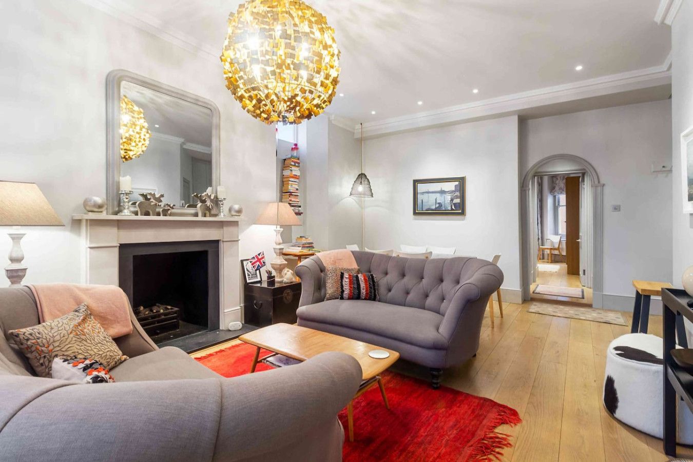 A modern living room with a fireplace, a grey sofa, a red rug, and a unique chandelier.