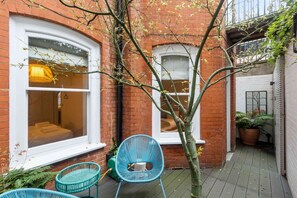 A narrow alleyway with a brick building, a small tree, and a blue chair.