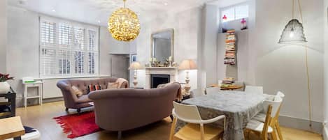 A modern living room with a sofa, dining table, and chairs, a fireplace, and a chandelier.