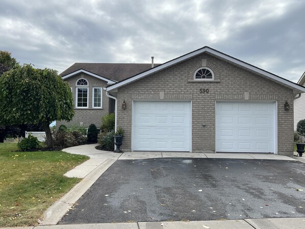 A two-story house with a brick facade, numbered 590, featuring two garage doors and a large tree in the front yard. - Arbour Ridge Vacation Home - Trail View! 5 bedrooms, 7 beds (Kingston)