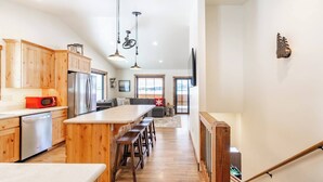 A spacious kitchen with wooden cabinets, a central island with bar stools, stainless steel appliances, and pendant lighting. - Fall Dates Available for Epic Sunsets (Anaconda)