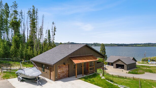 A lakeside cabin with a covered porch, a garage, and a boat docked outside. - Fall Dates Available for Epic Sunsets (Anaconda)