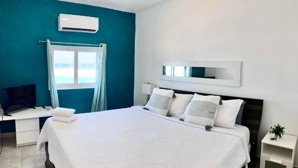 A hotel room with a large bed, a desk with a computer, a TV, and a window with curtains. - Casita Linda (Arecibo)