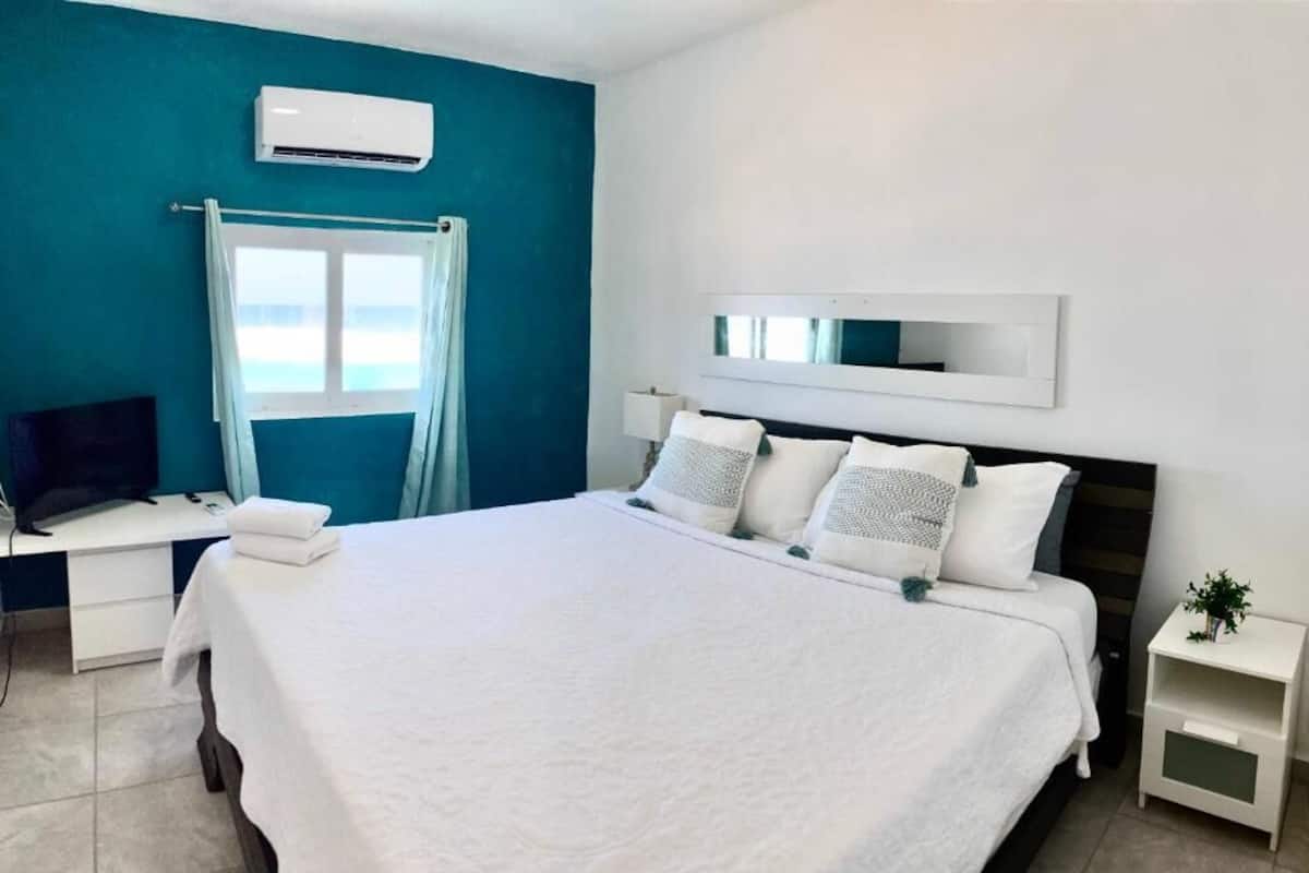 Habitación de hotel con una cama grande, un escritorio con computadora, un televisor y una ventana con cortinas.