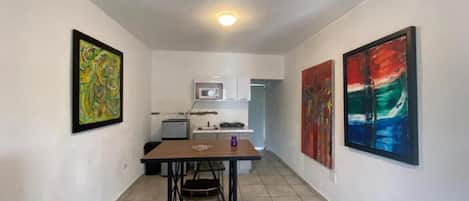 A narrow hallway with a dining table and chairs, a microwave, and cabinets in the background.